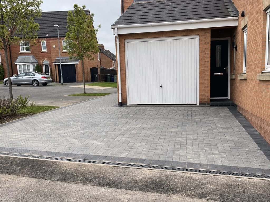 Grey block paving with a charcoal border and channel drain at a modern house in Dickens Heath