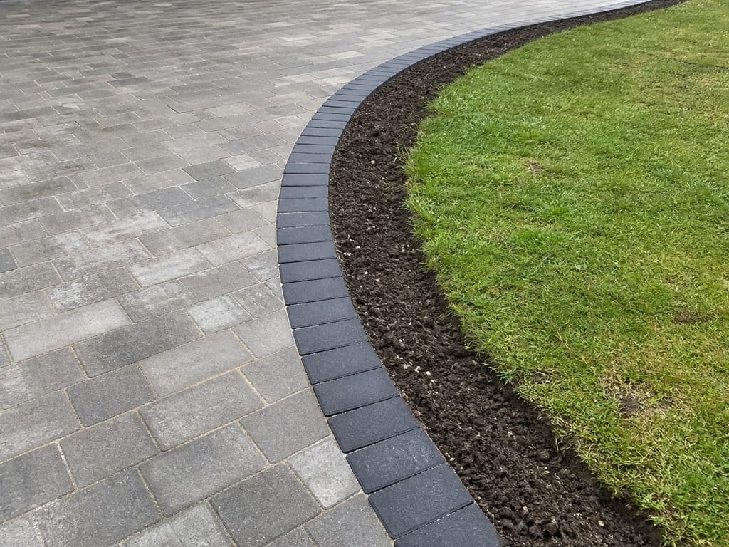 Curved charcoal border between block paving and a new lawn
